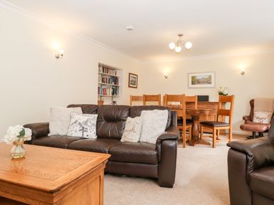 A living room with a brown leather sofa and wooden dining table with chairs at Holly Cottage in Grasmere
