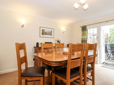 A dining room with a wooden table and chairs next to a sideboard and glass doors leading outside at Holly Cottage in Grasmere