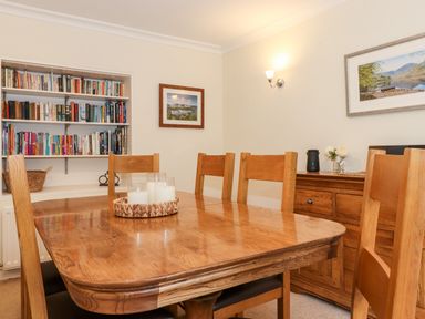 A dining room with a wooden table and chairs a bookshelf and framed pictures at Holly Cottage in Grasmere