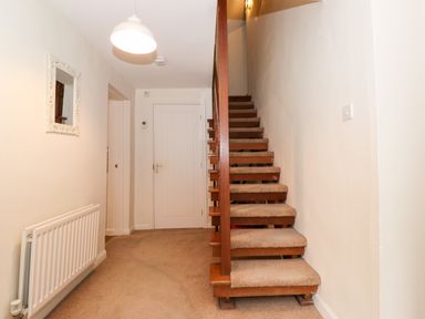A hallway with a carpeted staircase a door a radiator a hanging ceiling light and a mirror on the wall at Holly Cottage in Grasmere