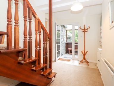 An entrance hall with wooden staircase coat stand and glass door leading outside at Holly Cottage in Grasmere