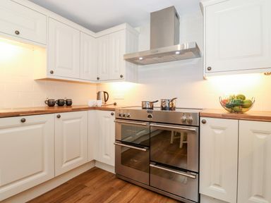 A kitchen with white cabinets stainless steel oven electric kettle and bowls on wooden countertops at Holly Cottage in Grasmere