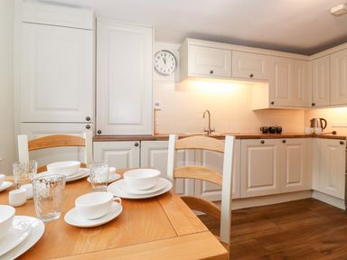 A kitchen with white cabinets a wooden dining table set with white dishes and glassware at Holly Cottage in Grasmere