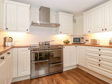 A kitchen with white cabinets a stainless steel stove and oven a microwave fruit bowl kettle and toaster on wooden countertops at Holly Cottage in Grasmere