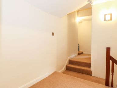 A carpeted staircase with beige walls and wooden handrail at Holly Cottage in Grasmere