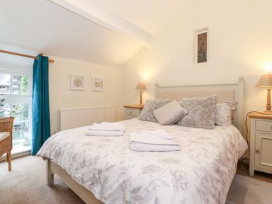 A bedroom with a double bed pillows side tables lamps and a window with blue curtains at Holly Cottage in Grasmere