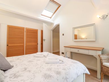A bedroom with a bed covered in floral bedding facing wooden closets under a skylight at Holly Cottage in Grasmere