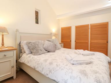 A bedroom with a double bed with grey pillows and white towels on the bed and wooden closet doors and bedside tables with lamps at Holly Cottage in Grasmere