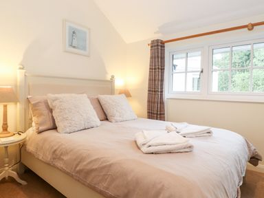 A bedroom with a double bed two lamps on bedside tables and a window with plaid curtains at Holly Cottage in Grasmere