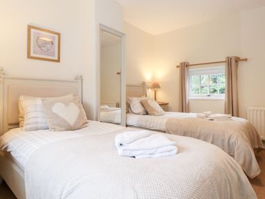 A bedroom with two single beds with beige bedding and pillows a window with curtains and a lamp on a bedside table at Holly Cottage in Grasmere