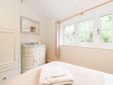 A bedroom corner with a cream cabinet a marble sink unit a mirror and a window with trees outside at Holly Cottage in Grasmere