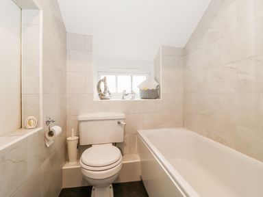 A bathroom with a toilet, bathtub, toilet brush, toilet paper holder, window ledge with decorative items at Holly Cottage in Grasmere