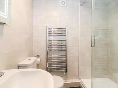 A bathroom with a toilet, sink, chrome towel radiator, and a glass shower enclosure at Holly Cottage in Grasmere