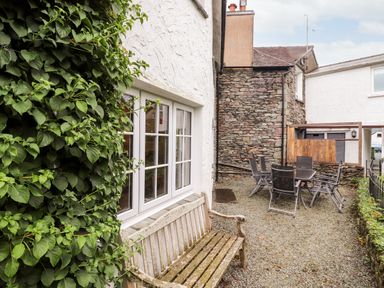 An outdoor seating area with a wooden bench near a window and a table with chairs on gravel near a stone wall