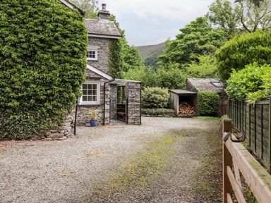 A stone cottage with ivy on the wall and a gravel driveway at Holly Cottage in Grasmere