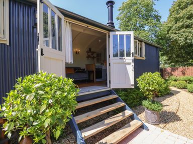 The exterior of a small building with double doors open showing a living area inside and steps leading to a garden path at Utopia in Metfield near Harleston