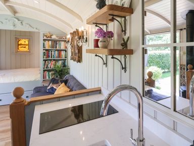 A small living area with a sofa and bookshelf next to a bed and kitchen countertop with sink and stove at Utopia Metfield near Harleston