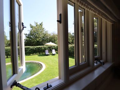 A view through open windows to a garden with a curved pond two lounge chairs and an umbrella at Utopia Metfield near Harleston