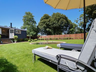 A garden with lounge chairs under an umbrella a small pond and a blue outdoor building at Utopia Metfield near Harleston