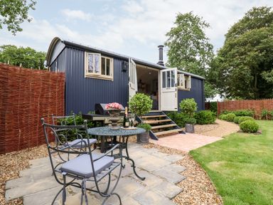 A garden with a metal table and chairs set on a stone patio outside a small blue cabin at Utopia in Metfield near Harleston