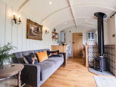 Living area with grey sofa and cushions next to wood burning stove and wooden door at Utopia Metfield near Harleston
