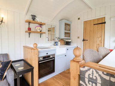 A small kitchen area with a blue oven and cabinets wooden shelves with decorative items and a wooden door at Utopia in Metfield near Harleston
