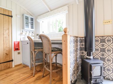 A kitchen corner with wicker bar stools wooden countertop wood stove with patterned tiles at Utopia in Metfield near Harleston