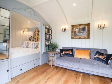 A room with a built in bed with a decorative headboard next to a gray sofa with pillows and a bookshelf at Utopia in Metfield near Harleston