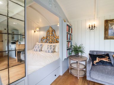 A bedroom with a bed having a carved headboard pillows a round wooden table with plant a bookshelf and a sofa with a rabbit cushion at Utopia Metfield near Harleston