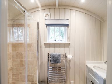 A bathroom with a glass door shower a small window above a towel rack and a sink cabinet at Utopia Metfield near Harleston