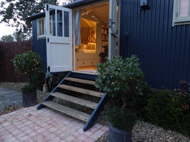 An open doorway with wooden steps leading to a bedroom inside a dark blue building with potted plants and string lights outside at Utopia in Metfield near Harleston