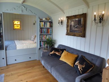 A living room with a gray sofa with decorative pillows and a bookshelf next to a bed area at Utopia in Metfield near Harleston