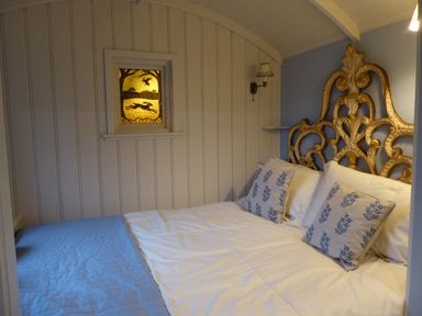 A bedroom with a bed with white and blue bedding and decorative pillows and a gold carved headboard at Utopia in Metfield near Harleston
