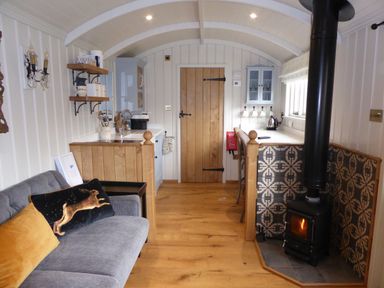 A small kitchen and living area with a wood stove a grey couch and wooden door at Utopia Metfield near Harleston
