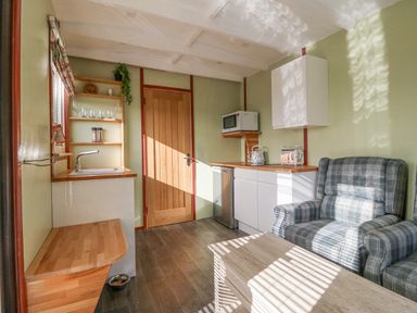 A small kitchen area with a wooden door plaid armchair wooden countertop and microwave at Nyth Y Bioden (Magpie's Nest) Llanaelhaearn near Trefor