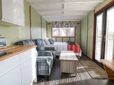 A small living area with a bed, two armchairs, a coffee table, kitchenette, and glass doors at Nyth Y Bioden (Magpie's Nest) in Llanaelhaearn near Trefor