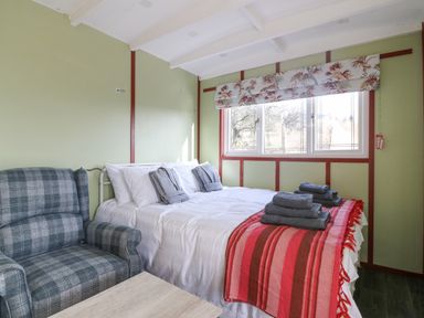 A bedroom with a bed covered in white linens and gray towels a plaid armchair and a window with floral blinds at Nyth Y Bioden (Magpie's Nest) in Llanaelhaearn near Trefor