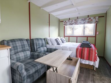 A bedroom with a bed with folded towels and a red blanket, two plaid armchairs, and a wooden coffee table at Nyth Y Bioden (Magpie's Nest) in Llanaelhaearn near Trefor