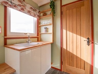 A kitchen sink with wooden countertop and open wooden shelves next to a wooden door at Nyth Y Bioden (Magpie's Nest) Llanaelhaearn near Trefor