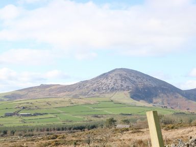 A rural landscape with a large mountain in the background green fields and a few buildings in the foreground at Nyth Y Bioden (Magpie's Nest) Llanaelhaearn near Trefor