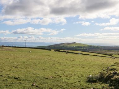 A grassy field with sheep and a hill in the background under a partly cloudy sky at Nyth Y Bioden (Magpie's Nest) Llanaelhaearn near Trefor