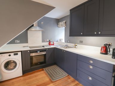 A kitchen with dark cabinets a white washing machine oven sink toaster and kettle at Grebe Cottage in Alnmouth
