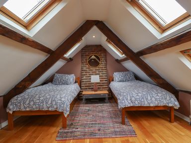 An attic bedroom with two single beds a wooden floor and skylights at Grebe Cottage in Alnmouth