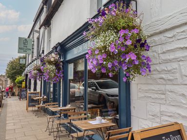 A street view of a tea room with hanging flower baskets and outdoor tables and chairs at Grebe Cottage in Alnmouth