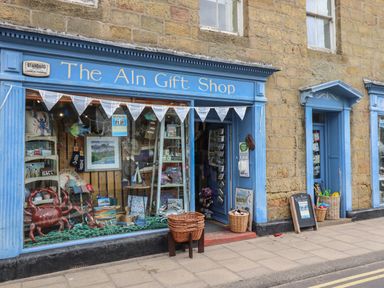 Front view of a blue shop with gift items displayed in the window on a stone building at Grebe Cottage in Alnmouth