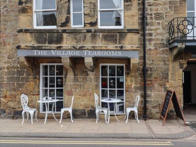 An outdoor seating area with white metal tables and chairs outside The Village Tearooms on a stone building