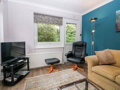 A living room with a black leather chair with footrest a yellow sofa a floor lamp and a television on a stand at The Lodge in Ambleside