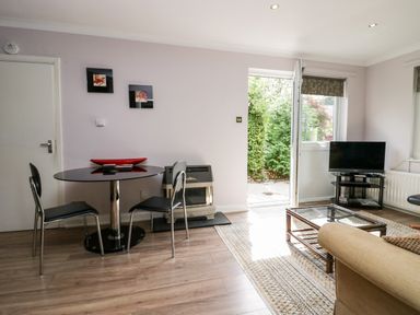 A living room with a round dining table and two chairs a television on a stand a glass coffee table and an open door to a garden at The Lodge in Ambleside