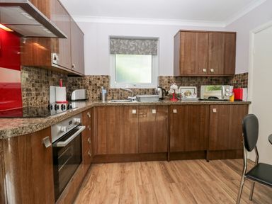 A kitchen with brown cabinets a window above the sink an oven a microwave and a black chair at The Lodge in Ambleside