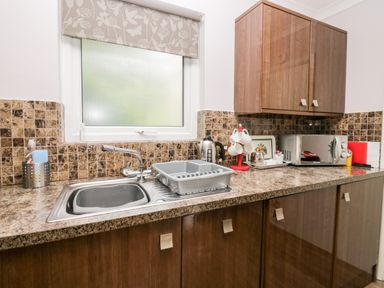 A kitchen countertop with a sink a drying rack a kettle a microwave and cabinets at The Lodge in Ambleside